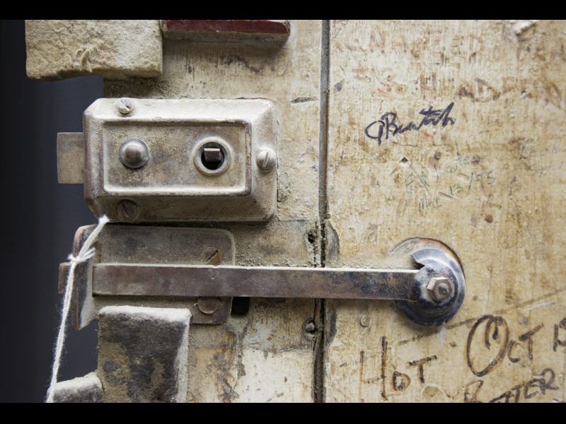 A worn two panelled grey-brown wooden door is covered with graffiti.